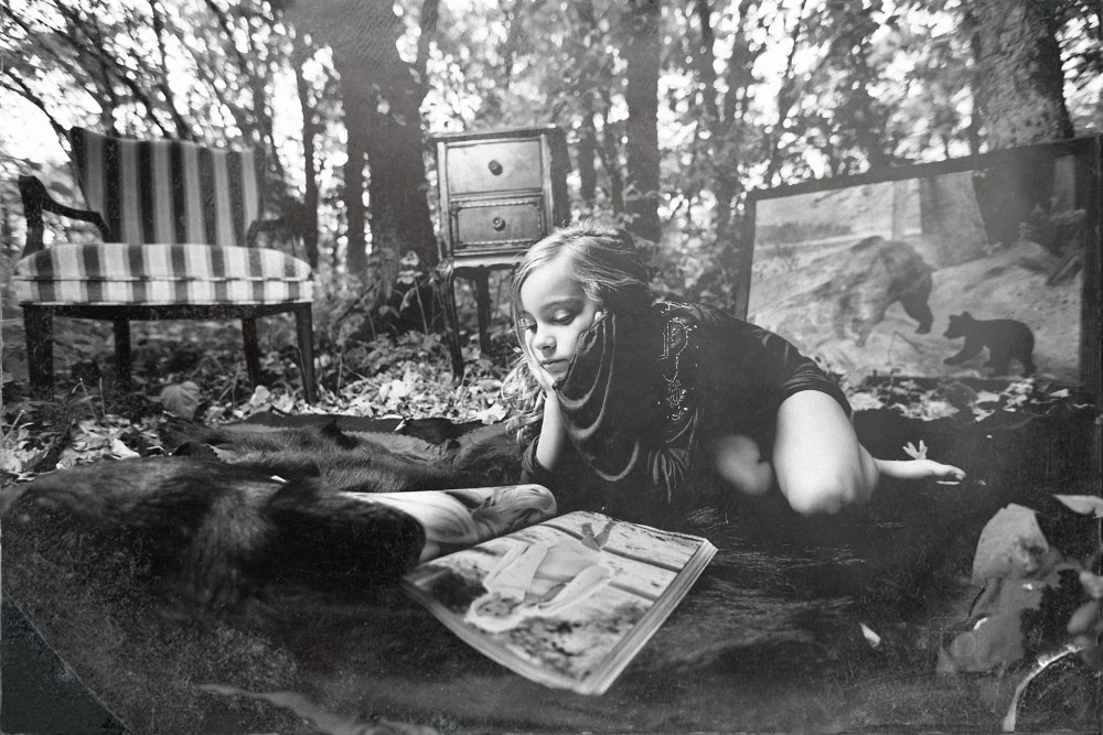 Teslyn on a bear rug in the woods reading Vogue magazine