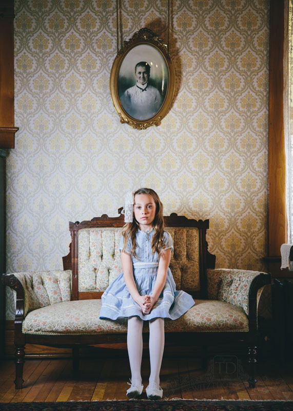 Teslyn sitting on antique sofa chair under vintage portrait