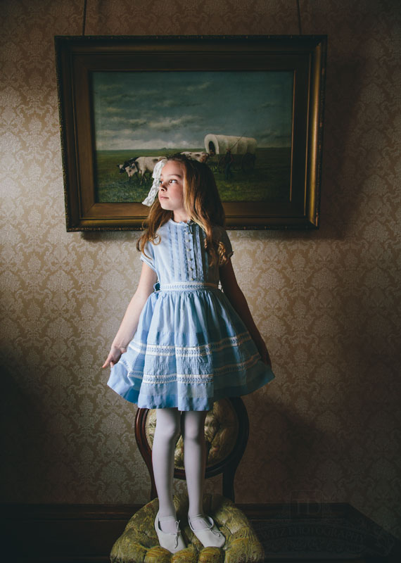 Teslyn standing on antique chair in front of painting looking out the window