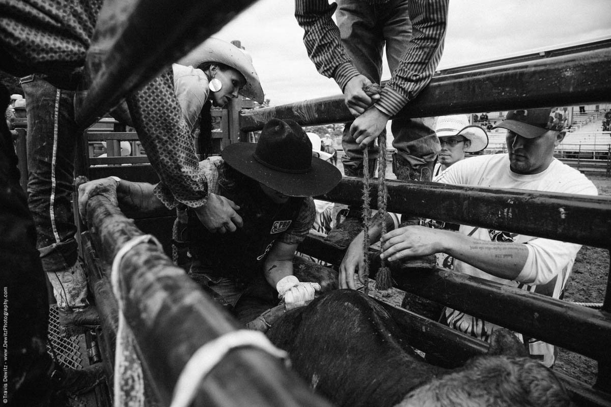 bull-rider-gets-strapped-on-bull-in-chute-black-cowboy-hat-black-river-falls-wi-rice-bull-riding-4816